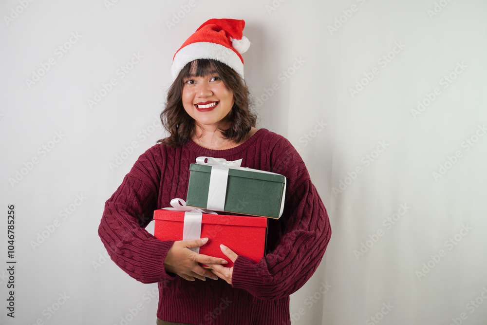 Excited young asian woman wearing santa clause hat and red long sleeved sweater is carrying large gift box with ribbon, isolated over white background. Concept for Christmas Holiday and New Year Party Excited young asian woman wearing santa clause hat and red long sleeved sweater is carrying large gift box with ribbon, isolated over white background. Concept for Christmas Holiday and New Year Party