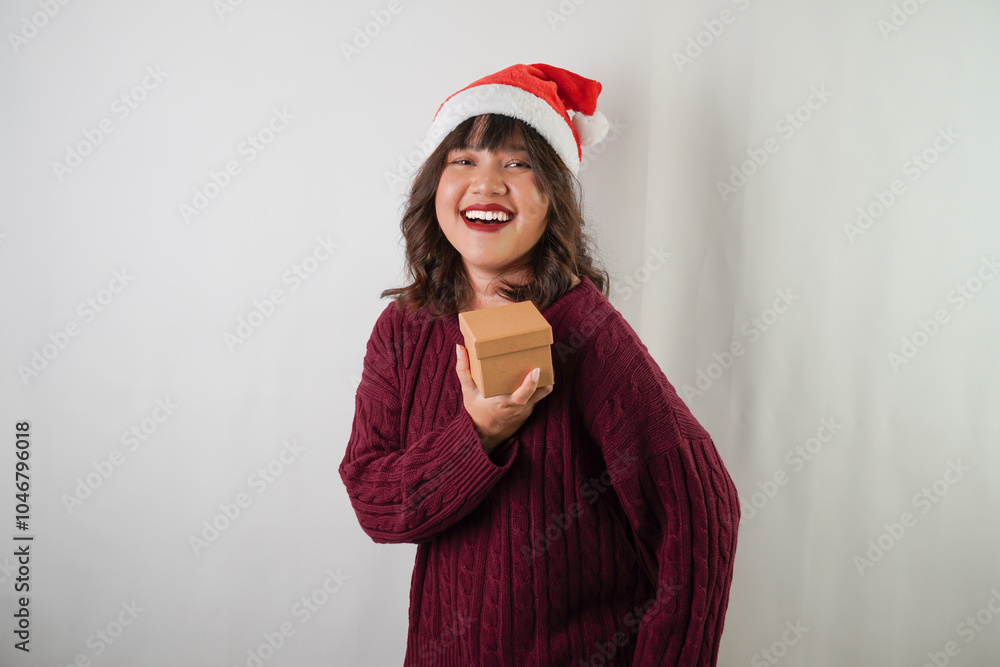 Excited young asian woman wearing santa clause hat and red long sleeved sweater is opening small gift box, isolated over white background. Concept for Christmas Holiday and New Year Party. Excited young asian woman wearing santa clause hat and red long sleeved sweater is opening small gift box, isolated over white background. Concept for Christmas Holiday and New Year Party.