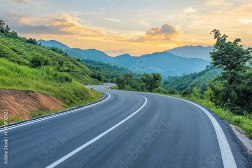 A winding asphalt road through lush green mountains at sunset.