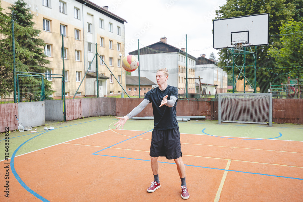 Fototapeta premium Volleyball player standing on a hard court, bouncing the ball while preparing for the next play during an outdoor game. A calm, focused moment before the action begins