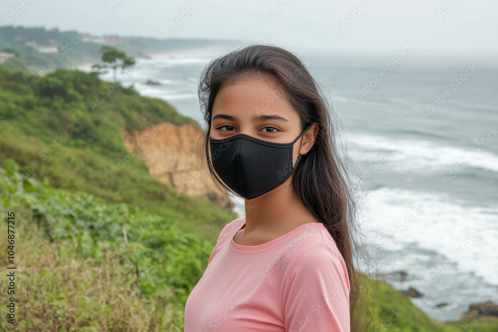 A young girl in a black face mask standing near a scenic ocean cliff, promoting safety and health A young girl in a black face mask standing near a scenic ocean cliff, promoting safety and health