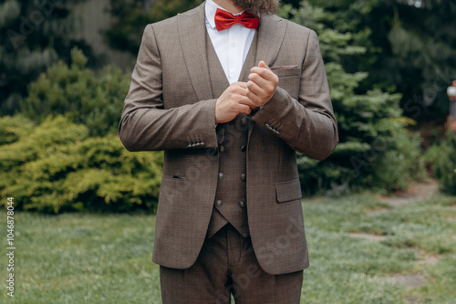 A man with  in a stylish suit  fixes a bow tie. Morning of the groom. Bride helps to fix the groom jacket and accessories