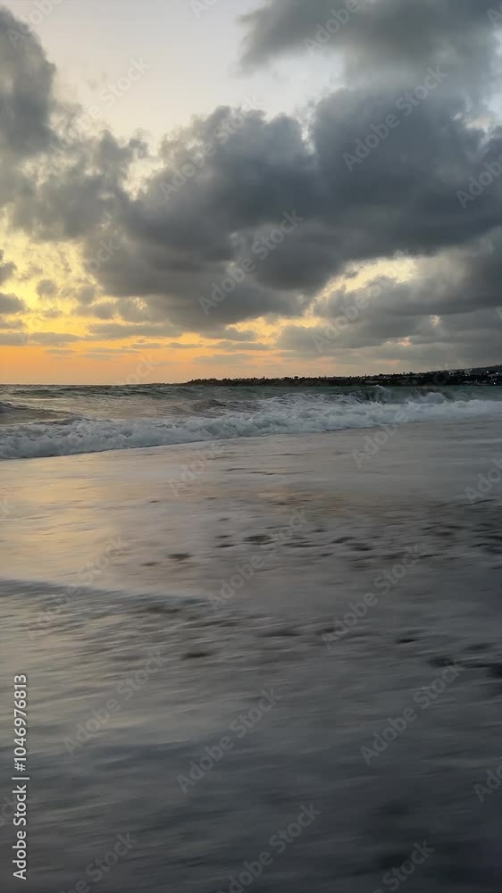 Low-angle view of ocean waves crashing onto a sandy beach at sunset, with dramatic clouds in the sky. Low-angle view of ocean waves crashing onto a sandy beach at sunset, with dramatic clouds in the sky.
