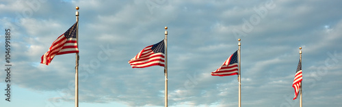 A panoramic row of four American flags stand tall, waving gracefully in the evenign breeze against a backdrop of a partly cloudy sky.