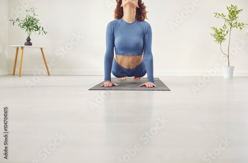 Young sporty woman practicing yoga, doing upward facing dog exercise, Urdhva mukha shvanasana pose, working out, wearing nice sportswear, white yoga studio, home laminate flooring clean surface photo