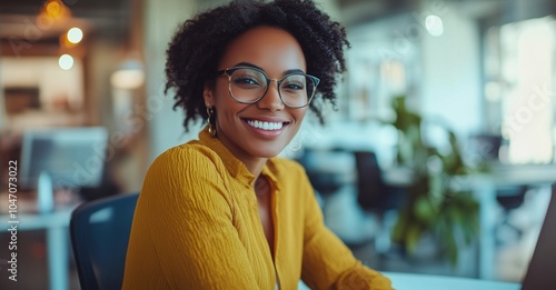 A woman wearing glasses and a yellow shirt is smiling at the camera