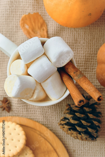 A warm winter drink is topped with marshmallows, cinnamon sticks, and holiday decorations on a cozy surface