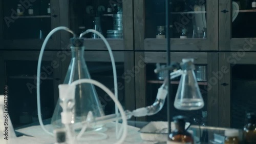 A large old style chemistry lab with lots of beakers, test tubes, flasks, spirit lamps, chemicals and other chemical equipment on a large glass table. Closeup. Macro. Shot in motion