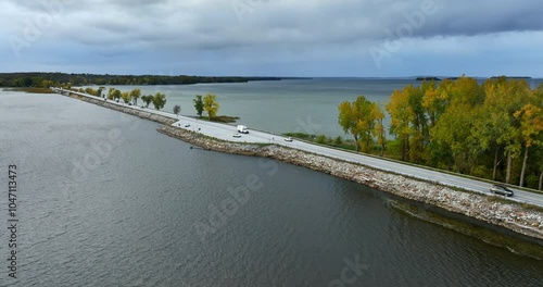 Cars riding by the highway built along the lake. Waterscape of Lake Champlain, Vermont, New England, USA. Grey day on the lake. photo