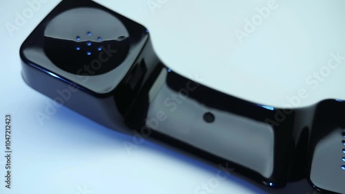 Shiny black handset with cable of old push-button telephone shines in darkness on white and black background. Closeup. Macro. Shallow depth of field. Shot in motion