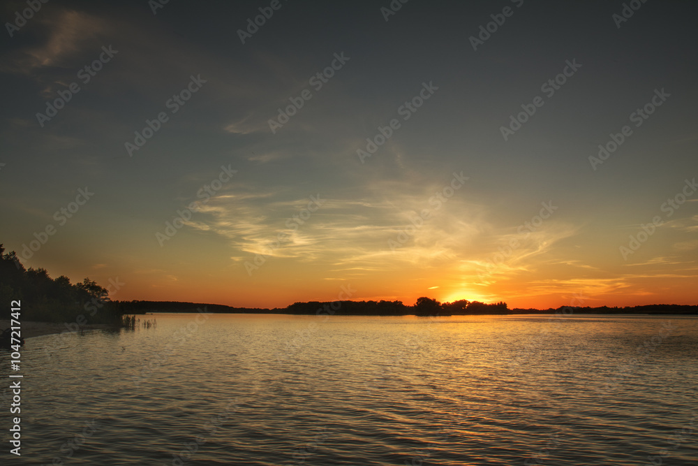 Obraz premium Golden sunset illuminating calm lake with cirrus clouds creating a serene atmosphere