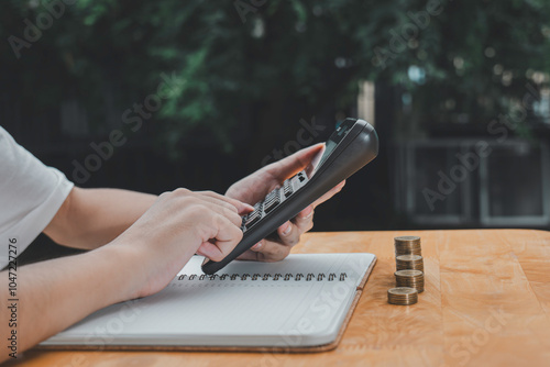 Young businessman using calculator and expenditure into notebooks and putting coins in piggy banks to save money invest for future.Concept for loan,property,financial,estate investment,taxes and bonus