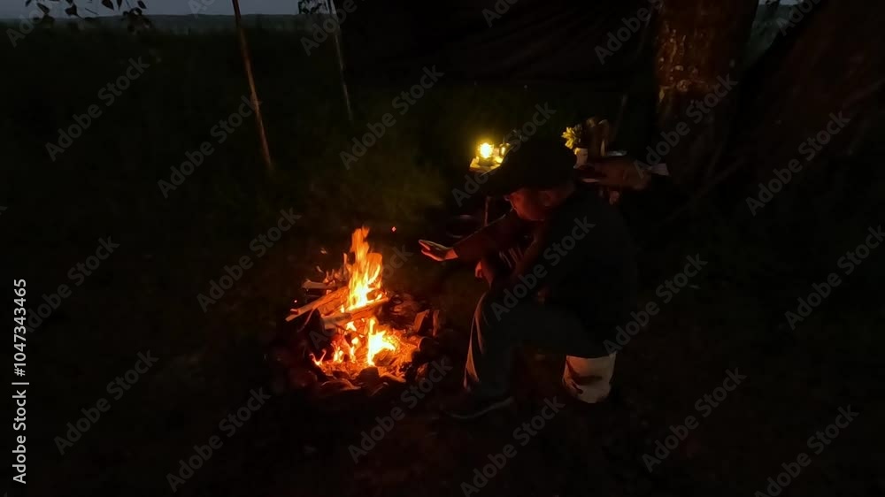 A man sits by a fire at night in the forest A man sits by a fire at night in the forest