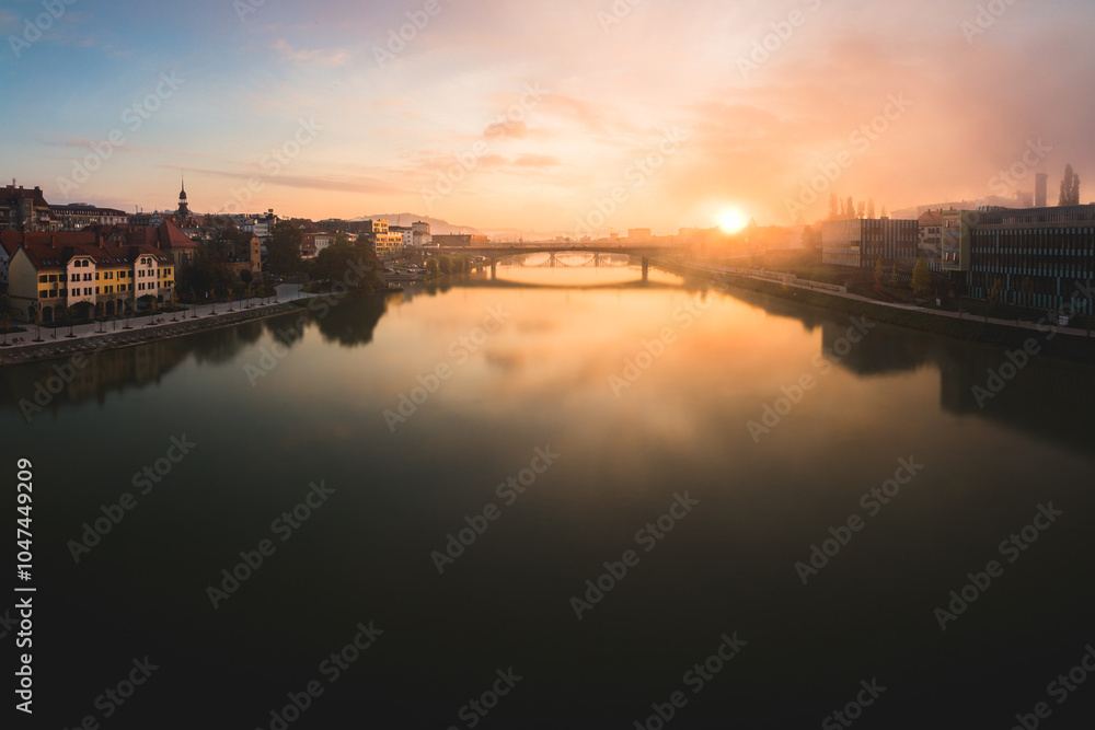Obraz premium Maribor city at sunrise with fog over the river Drava. There is a bridge over the river