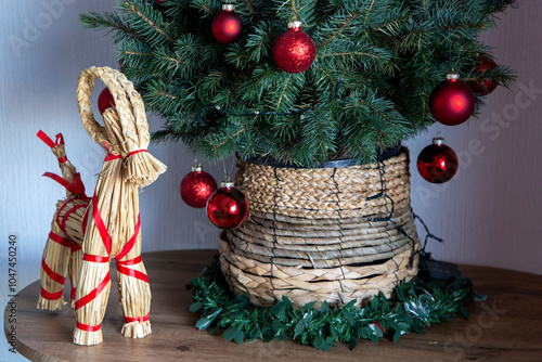A Scandinavian-inspired Christmas display featuring a red-decorated artificial tree in a straw pot, accompanied by a traditional Yule Goat.