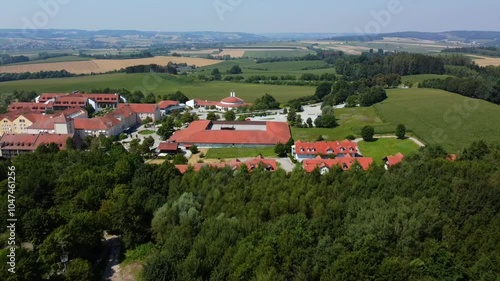 Aerial footage of Bad Griesbach Therme in Lower Bavaria, showcasing the spa complex with red-roofed buildings, surrounded by lush green fields and rolling hills. photo