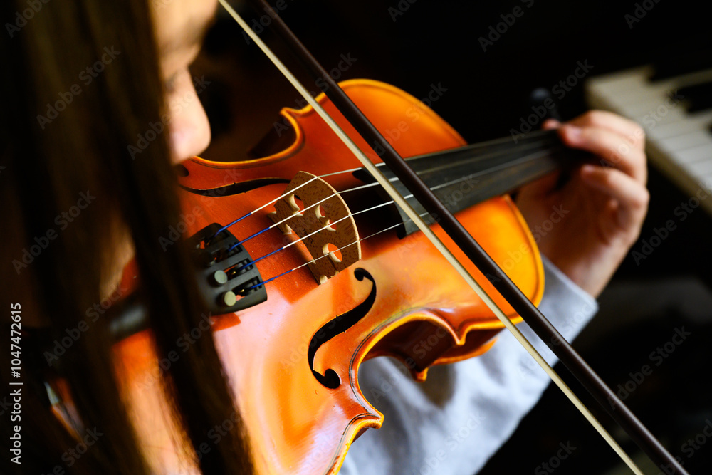 Closeup of a young dark-haired girl playing a violin next to piano keys Closeup of a young dark-haired girl playing a violin next to piano keys