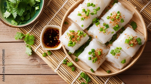 Steamed rice noodle rolls (Cheung Fun), placed on a light bamboo mat, garnished with soy sauce, chopped green onions, and fresh cilantro photo