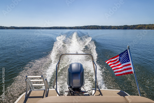 Boat wake behind boat on freshwater lake. American flag flying behind pontoon party boat.