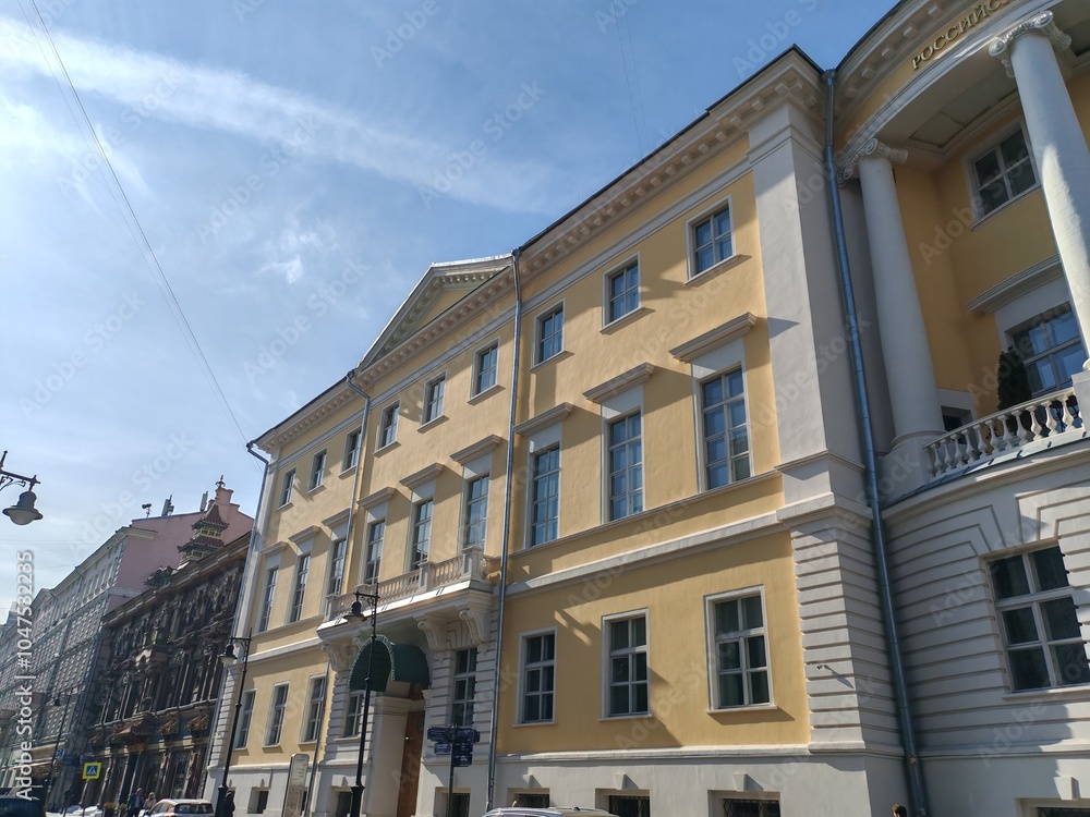 Naklejka premium grand yellow building with symmetrical windows and classical detailing, featuring a decorative arched entrance. The clean facade highlights the elegance of traditional urban architecture under a clear