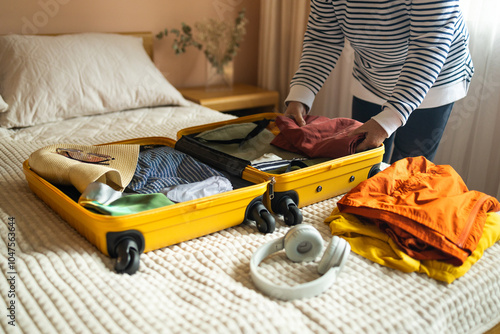 Obraz na płótnie Woman packing suitcase on bed for a new journey packing list for travel planning preparing vacation. Open yellow suitcase with different family clothes and accessories on sofa. w salonie