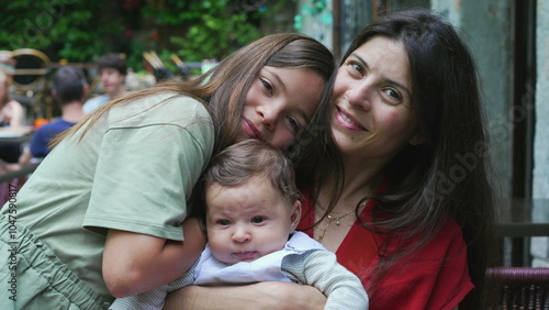 Mother and her two children sharing a warm embrace outdoors. Young girl hugs her mother and baby sibling, expressing love and closeness in a relaxed and joyful family moment
