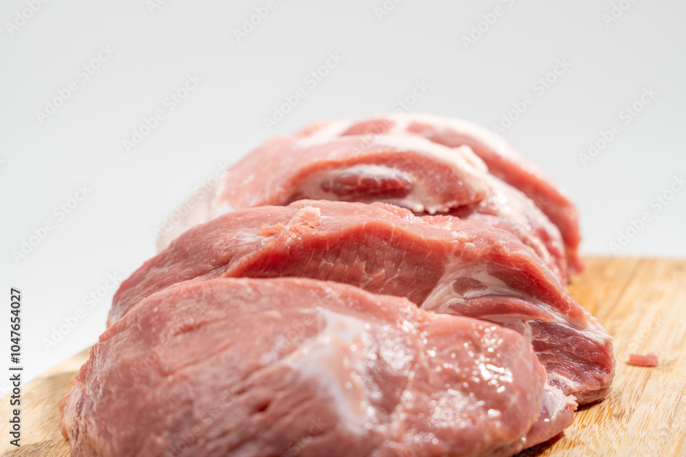 A slab of meat is cut into slices and placed on a wooden cutting board. Concept of preparation for cooking or serving the meat Pork meat isolated on a white background.