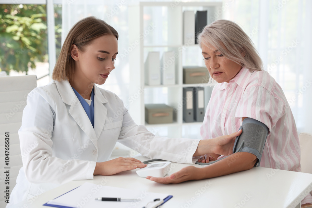 Doctor measuring patient's blood pressure at table in hospital Doctor measuring patient's blood pressure at table in hospital