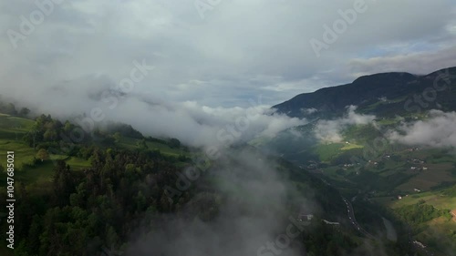 Serene aerial view of fog rolling over a picturesque mountain valley with green hills and winding roads below. photo