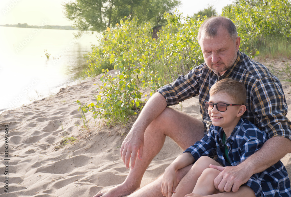 Father's day concept. Father and son sit together on the river bank and look into the distance.