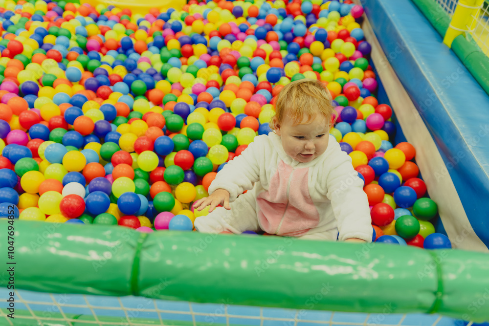 Obraz premium A young child is having fun exploring a vibrant ball pit filled with a multitude of colorful plastic balls in an indoor play space.