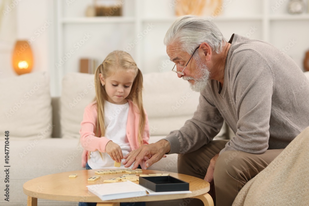 Grandpa and his granddaughter playing dominoes at table indoors Grandpa and his granddaughter playing dominoes at table indoors
