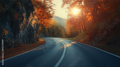 Winding road through an autumn forest with the sun setting behind the trees.