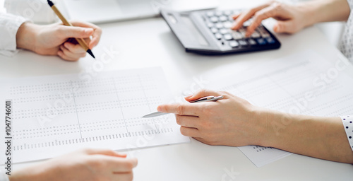 Accountant using a calculator and laptop computer for counting taxes with a client or a colleague at white desk in office. Teamwork in business audit and finance photo