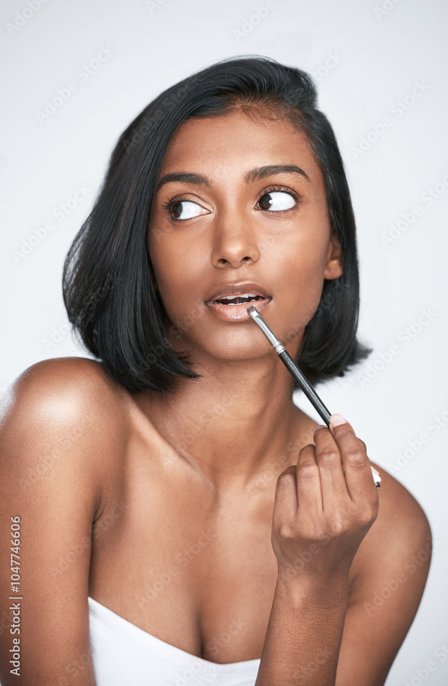 Indian woman, beauty and makeup with thinking, idea and lip gloss in wellness, routine or facial treatment. Female person, serious and planning for cosmetics, dermatology or glow on studio background Indian woman, beauty and makeup with thinking, idea and lip gloss in wellness, routine or facial treatment. Female person, serious and planning for cosmetics, dermatology or glow on studio background