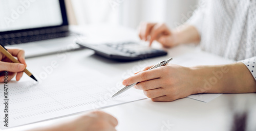 Two accountants using a laptop computer and calculator for counting taxes at white desk in office. Teamwork in business audit and finance