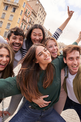 Vertical. Tourist group of young excited friends together posing happy for photo in city. Gen z people smiling with arms raised in air for holiday souvenir picture enjoying having fun in European town photo