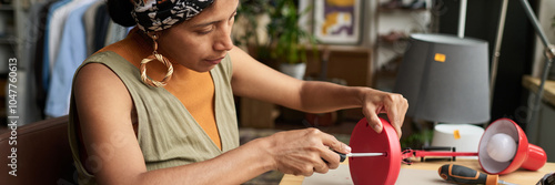 Quadro su tela Banner of young stylish female worker of thrift shop fixing screws in electric l