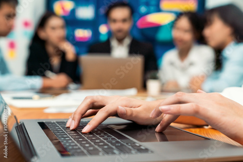 Closeup hand typing keyboard laptop with blurred background of business people using laptop to analyze financial data or data analysis display on screen background. Meticulous