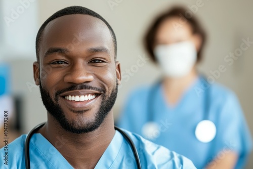 A smiling black man in a blue scrubs shirt is standing in front of a woman weari photo