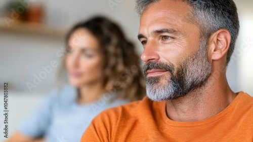 A middle-aged man with a salt-and-pepper beard gazes thoughtfully forward, wearing an expressive orange t-shirt, embodying introspection and vitality in calm setting. photo