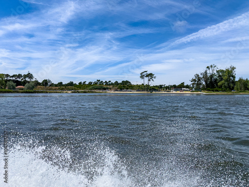 A view of the calm riverside river with soft splashes of water against the shore beneath a bright blue sky.  Areinho beach in Ria de Aveiro, Ovar - Portugal. photo