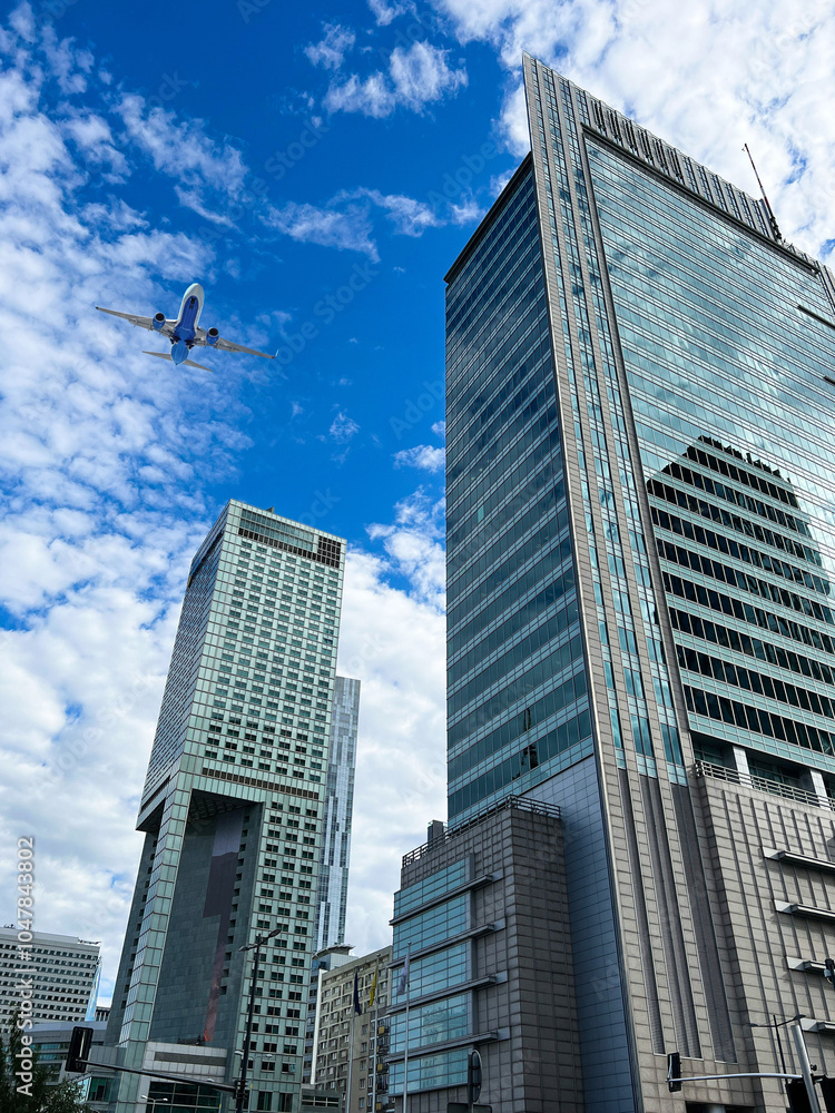 Obraz premium Airplane flying over buildings in city, low angle view