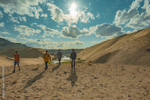 A group of friends on the background of the sand of the sky and the river on the slope. The travelers are walking towards the camera. Tourists walk along the sand against the background of the sky and