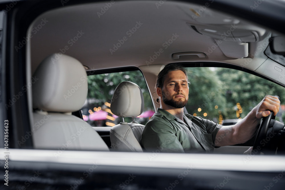 A young man in a car looking relaxed while driving in a city environment A young man in a car looking relaxed while driving in a city environment