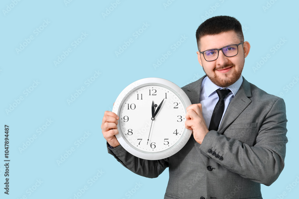 Young happy businessman with clock on blue background. Time management concept Young happy businessman with clock on blue background. Time management concept