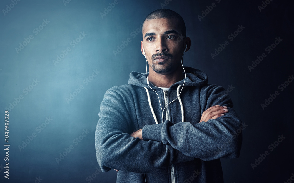 Man, arms crossed and hoodie in studio for fitness with thinking, workout and earphones by dark background. Person, music and mock up space to start training, listen and exercise routine for health Man, arms crossed and hoodie in studio for fitness with thinking, workout and earphones by dark background. Person, music and mock up space to start training, listen and exercise routine for health