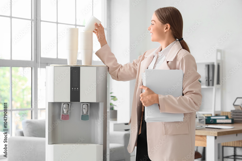Young businesswoman taking paper cup from water cooler in office Young businesswoman taking paper cup from water cooler in office