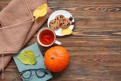 Composition with warm sweater, cup of tea, book and pumpkin on wooden background