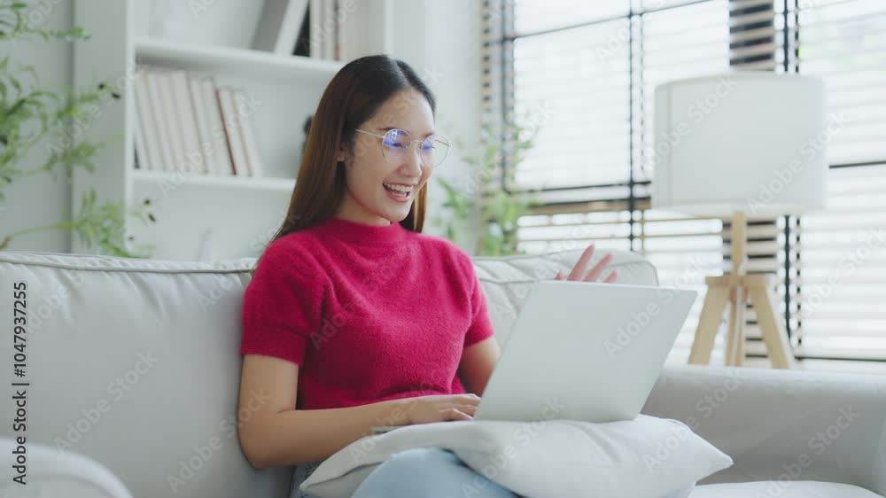 Happy young Asian woman using laptop while seated on couch at home Happy young Asian woman using laptop while seated on couch at home